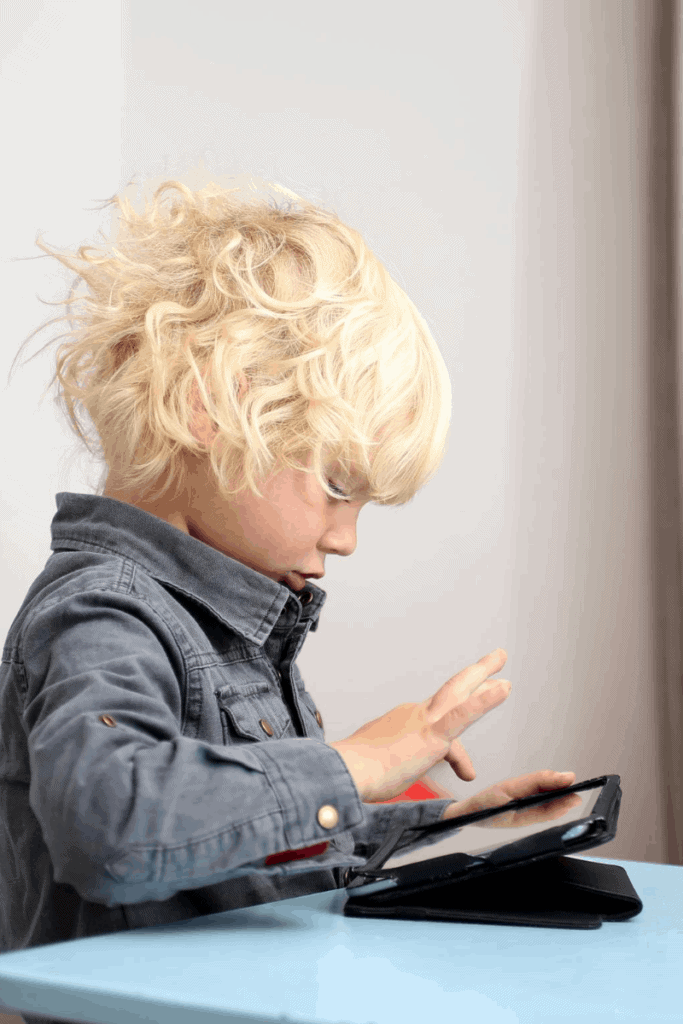A boy playing on a tablet sitting on a blue table. 
