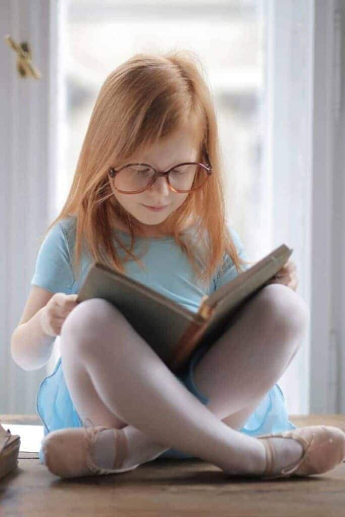 Child sitting cross legged focusing on a book and learning how to read from home.
