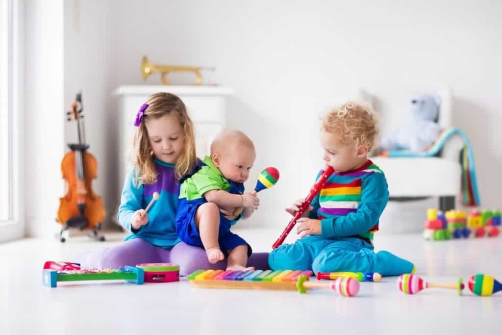 a baby and two toddles sit on the floor playing with colorful music instruments exploring activities