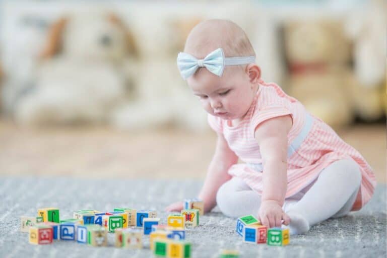 a baby sits on a rug playing with blocks as a part of a pincer grasp activity