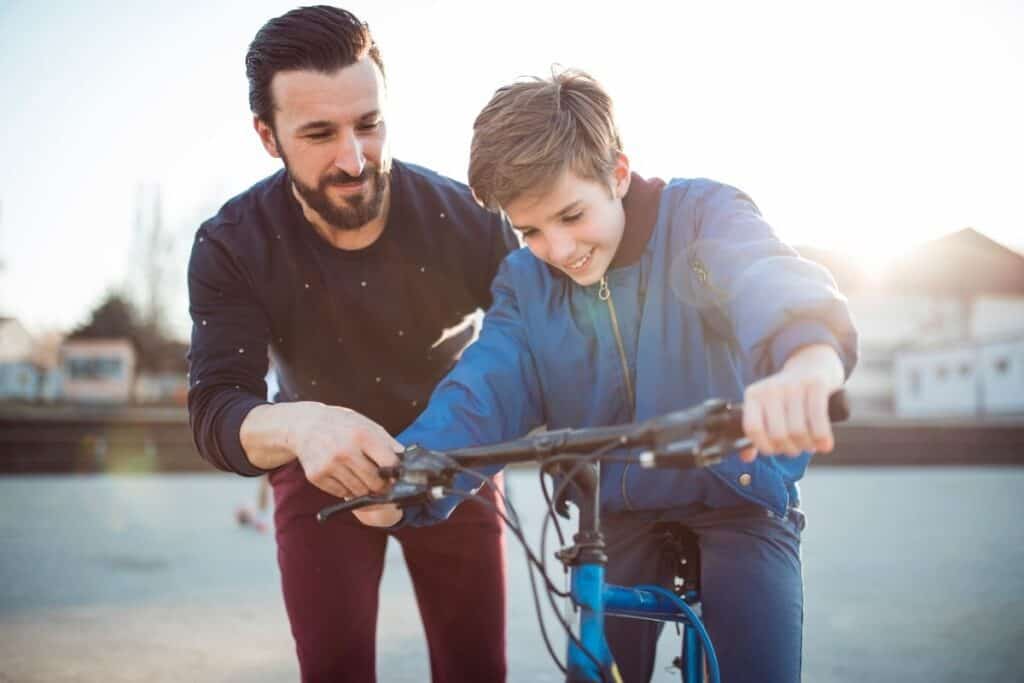 a dad helping his son learning how to ride a bike displaying the qualities of a good parent