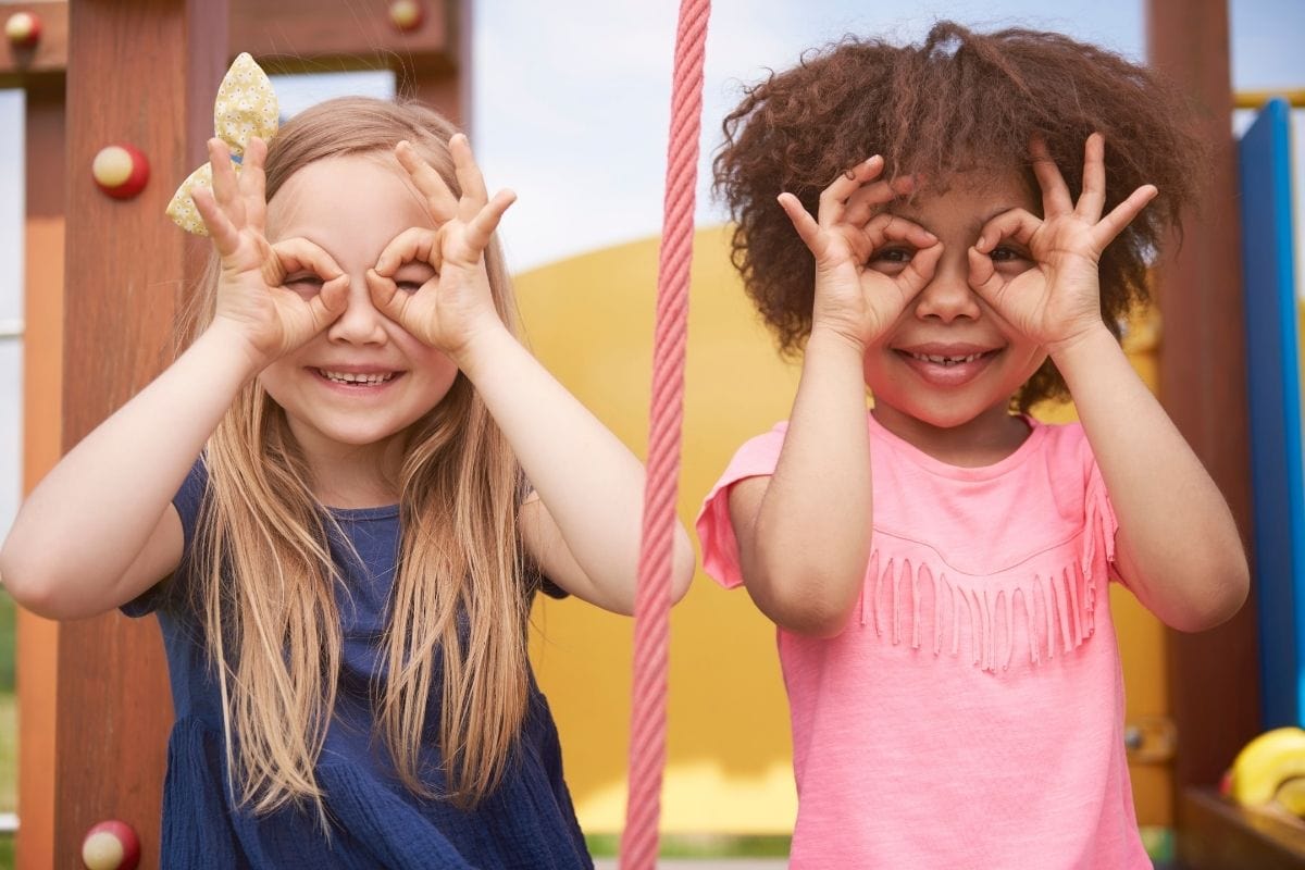 Two children side by side playing with their hands as pretend eye glasses.