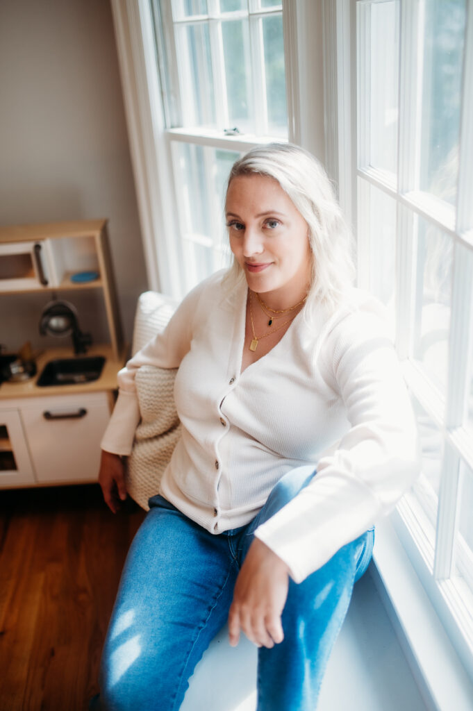 blonde woman sitting on window sill looking straight at the camera