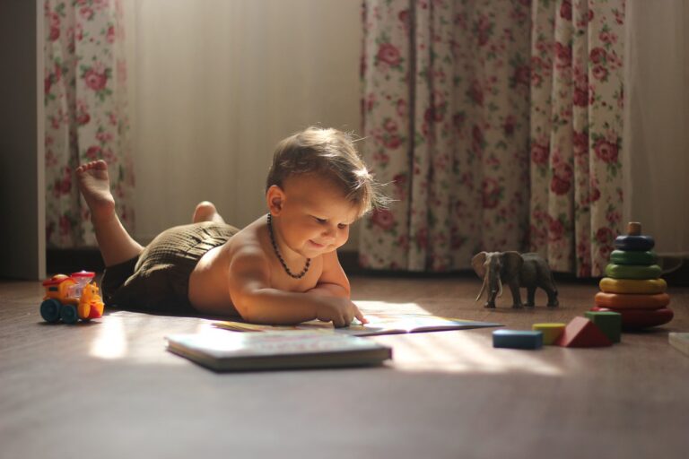 Toddler laying on his stomach in a living room reading a book