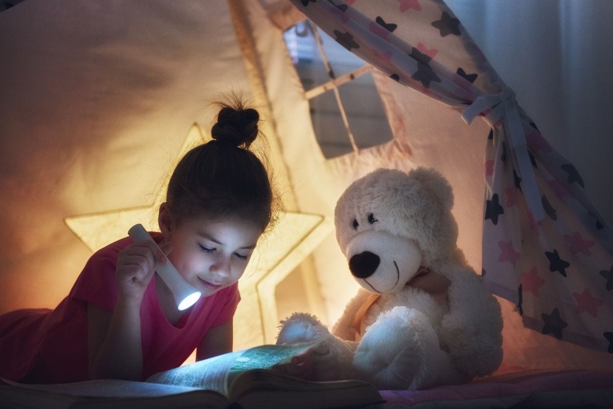 Young child using a flash light to read in bed.