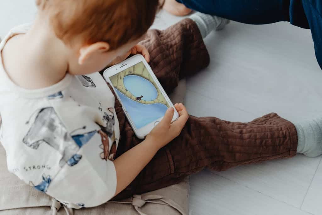 A young child playing an educational game on a smartphone indoors, focused on learning.