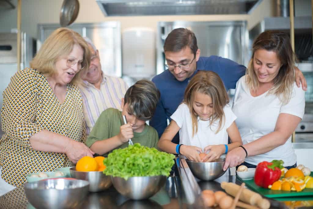 Family of various ages gathers in kitchen to cook meal together, showcasing culinary togetherness.