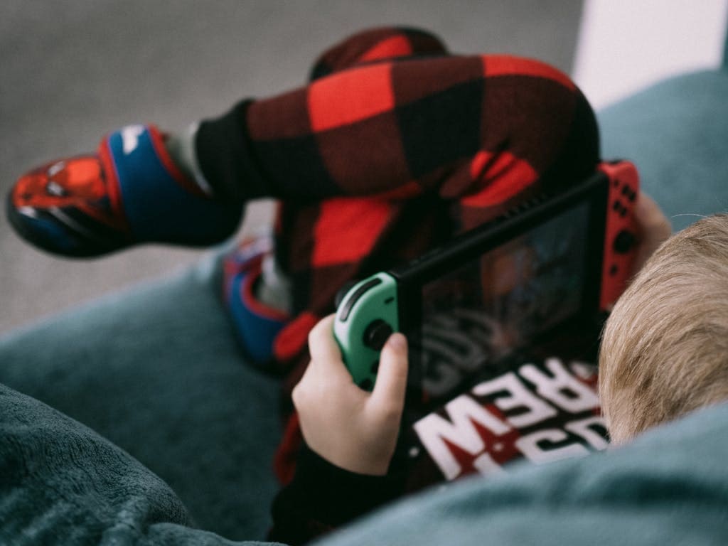 Young boy sitting on a sofa playing video games on a handheld console, enjoying leisure time.